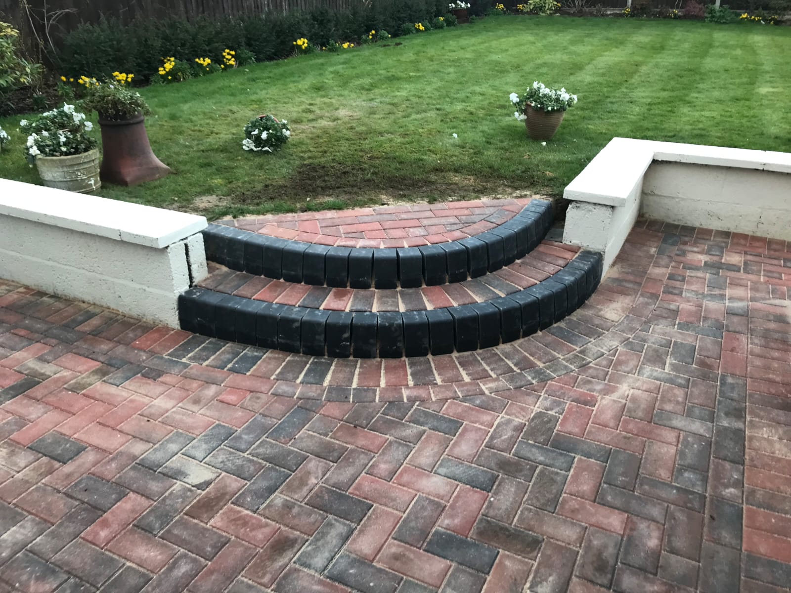 Red and charcoal herringbone patio with curved charcoal steps up to the lawn