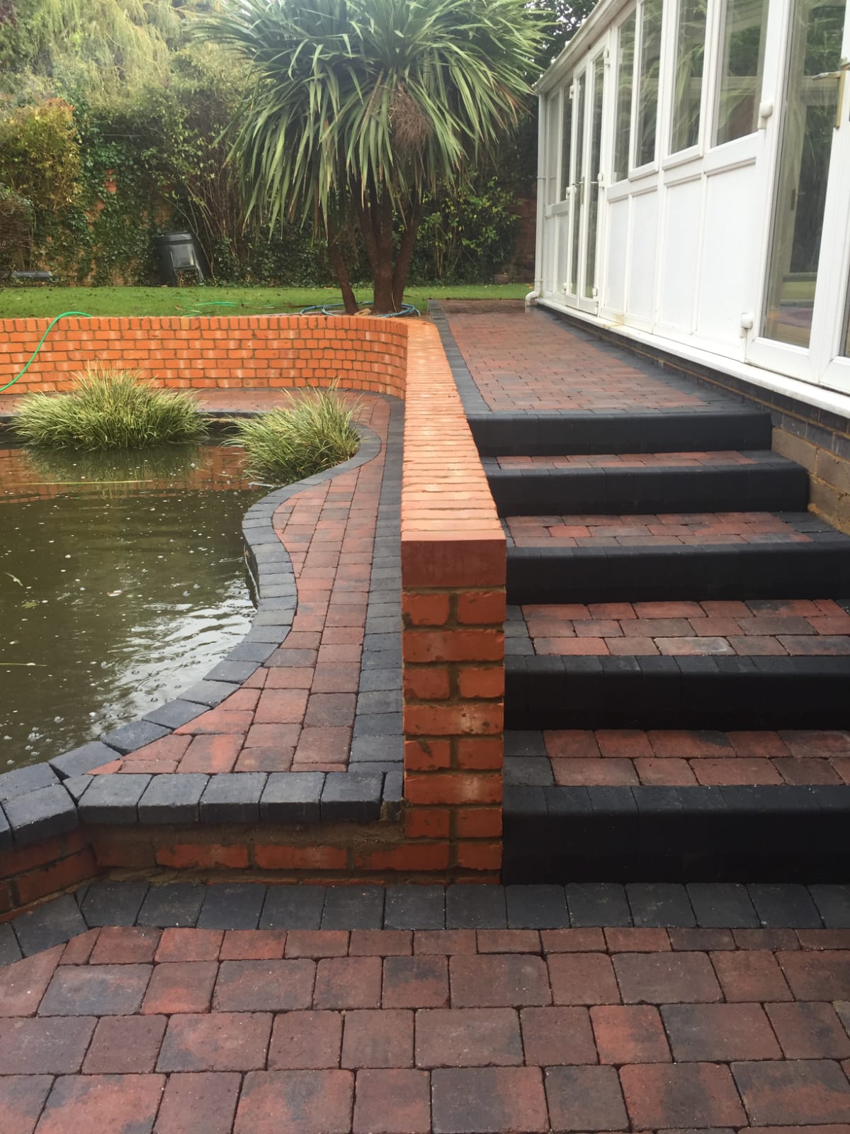 Brick steps and a curved brick pond wall above new block paving
