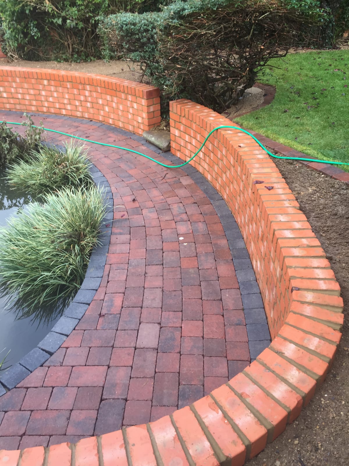 Curved red brick garden wall alongside a red block-paved path