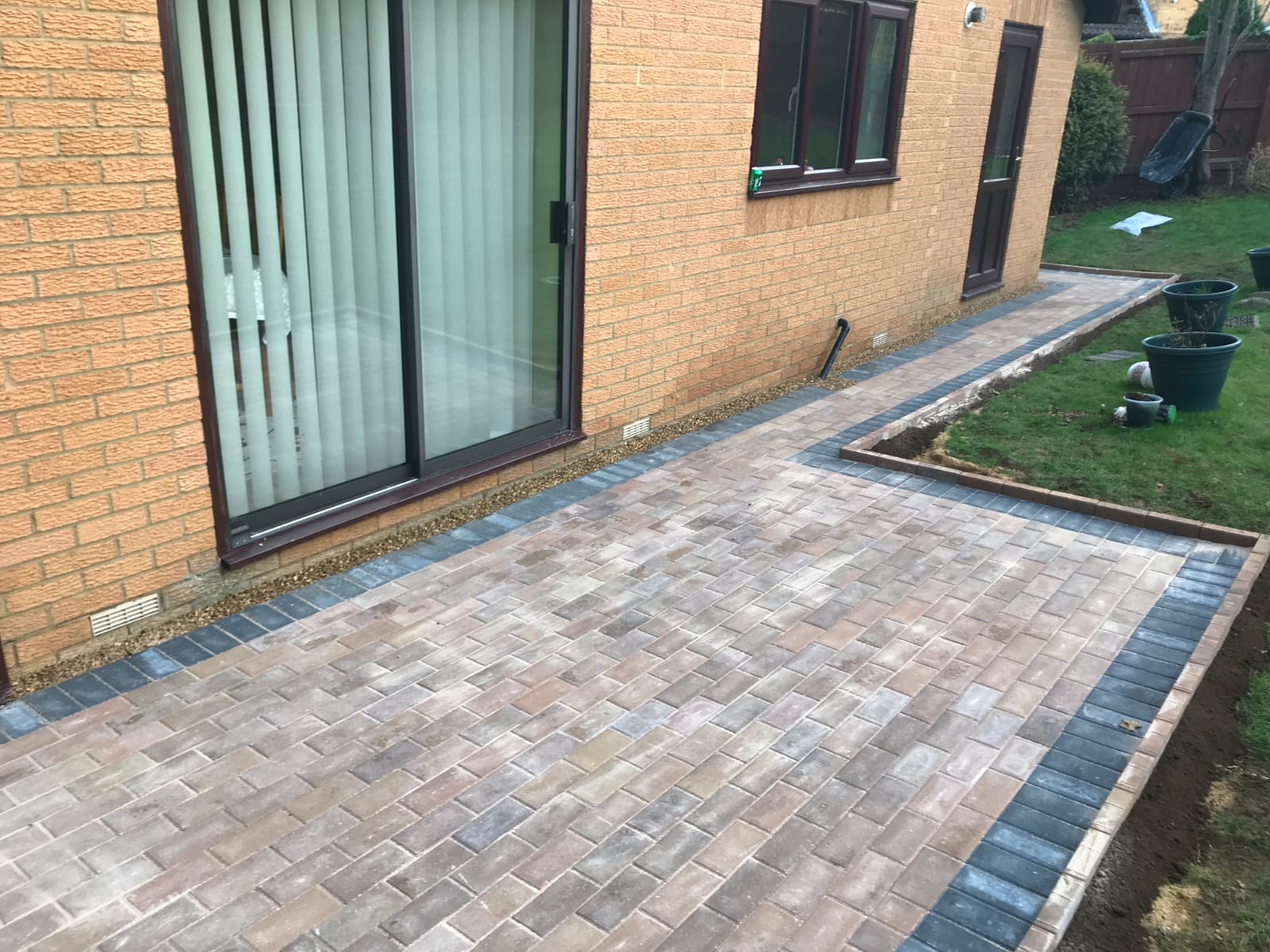 Light block-paved patio with a charcoal border beside a bungalow